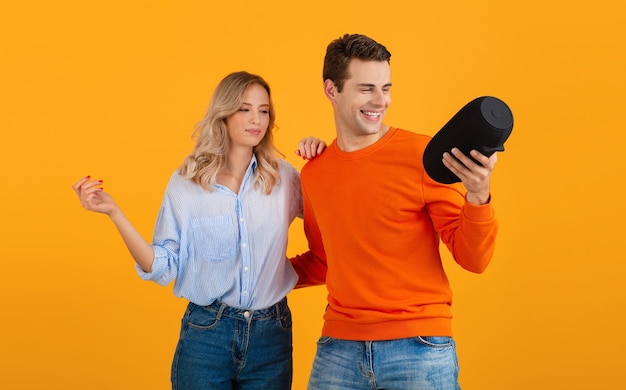 Beau jeune couple souriant tenant haut-parleur sans fil écouter de la musique dansant sur orange