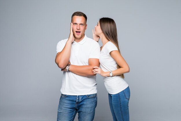 Beau jeune couple surpris en t-shirts blancs et jeans ayant une conversation secrète