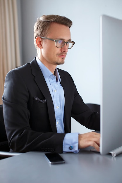 Beau jeune homme d'affaires travaillant avec un ordinateur au bureau.