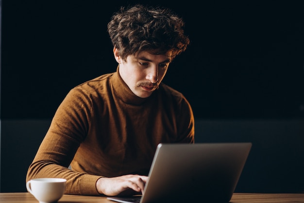 Beau jeune homme d'affaires travaillant sur ordinateur et boire du café