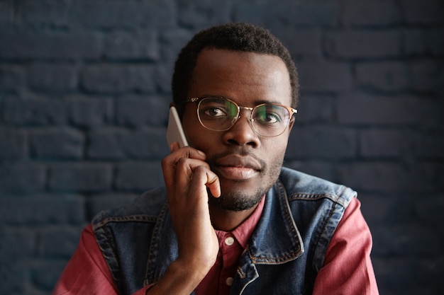 Beau jeune homme africain portant des lunettes élégantes parler au téléphone mobile avec sa petite amie, l'attend