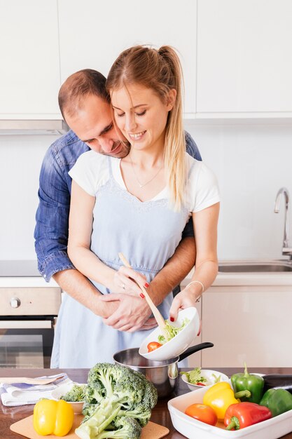 Beau jeune homme aimant sa femme préparant la nourriture dans la cuisine