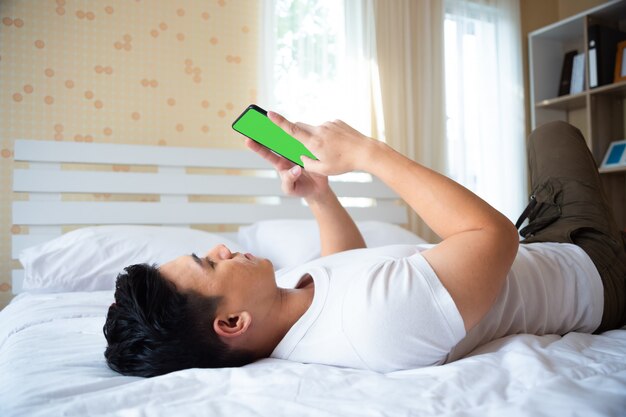 Beau jeune homme allongé sur lit et utilisation smartphone