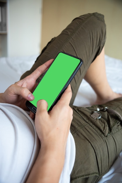 Beau jeune homme allongé sur lit et utilisation smartphone