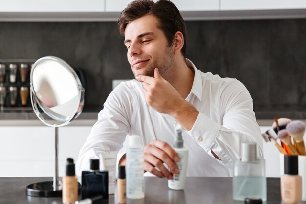 Beau jeune homme appliquant des produits de maquillage et de beauté