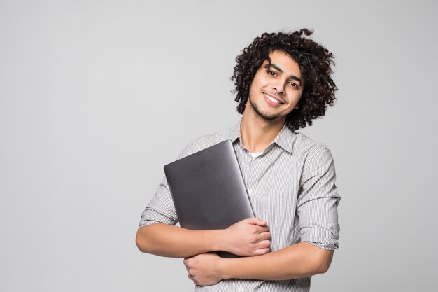 Beau jeune homme aux cheveux bouclés travaillant sur ordinateur portable debout isolé sur mur blanc,