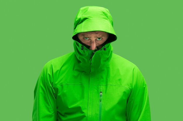 Beau jeune homme barbu de congélation isolé sur une couleur verte à la mode vive au studio. concept de l'apparition de l'automne et du froid