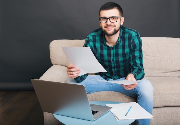 Beau jeune homme barbu hipster assis sur un canapé à la maison