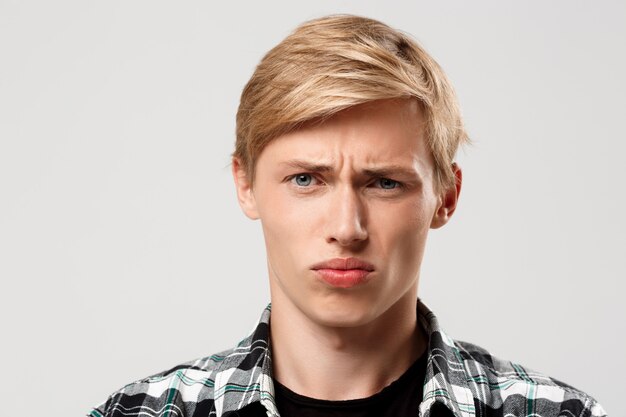 Beau jeune homme blond confiant portant une chemise à carreaux décontractée sur le mur gris