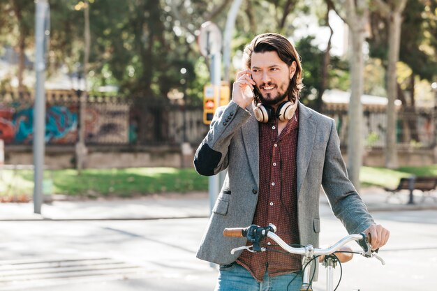 Beau jeune homme avec un casque autour du cou parlant au téléphone sur la route