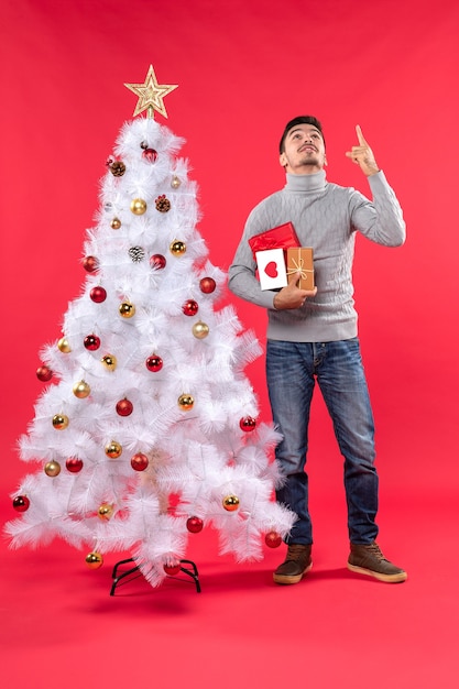 Beau jeune homme debout près de l'arbre de nouvel an blanc décoré