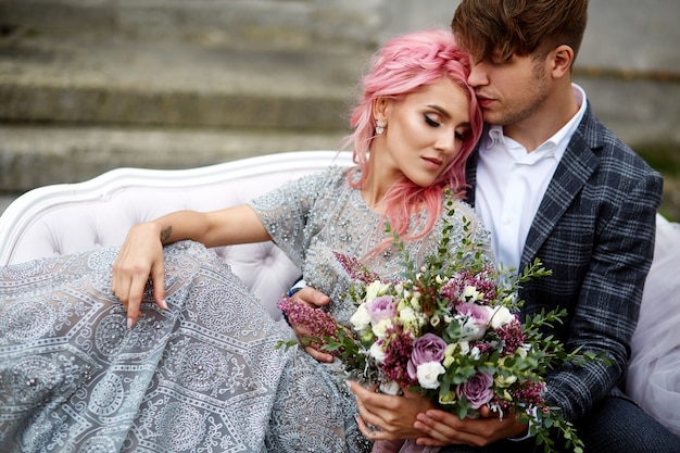 Beau Jeune Homme Embrasse Une Femme Tendre Avec Des Cheveux Roses, Assis Sur Le Canapé Blanc