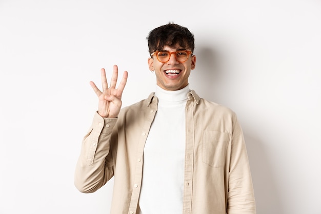 Beau jeune homme faisant l'ordre, montrant le numéro quatre doigts et souriant, debout sur fond blanc.