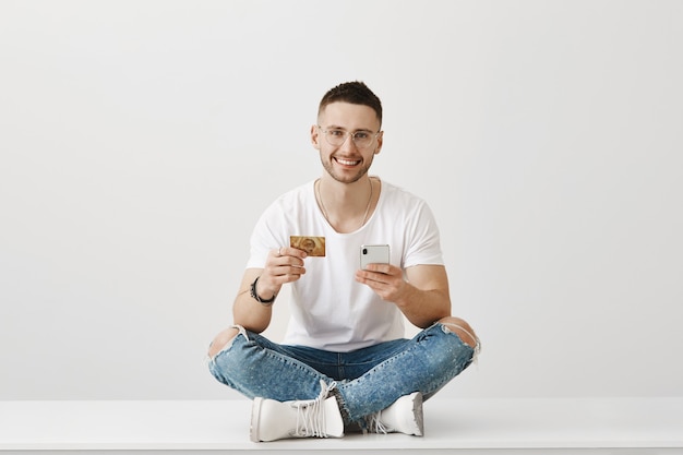 Beau jeune homme avec des lunettes posant avec son téléphone et sa carte