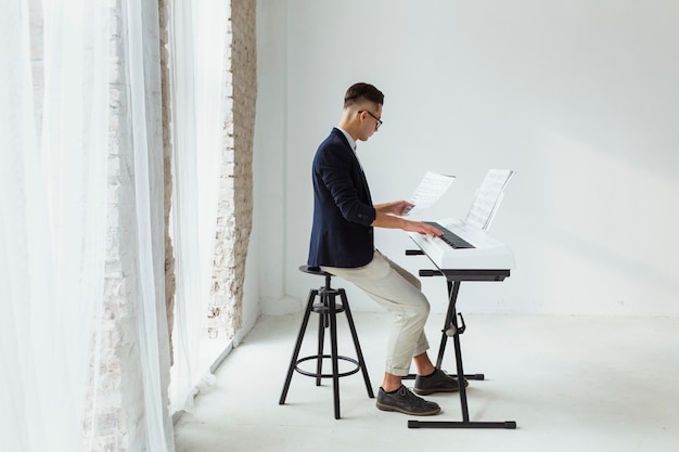 Beau, jeune homme, manteau, regarder, feuille musicale, jouer, clavier