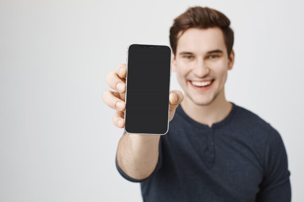 Beau jeune homme montrant l'affichage du téléphone mobile