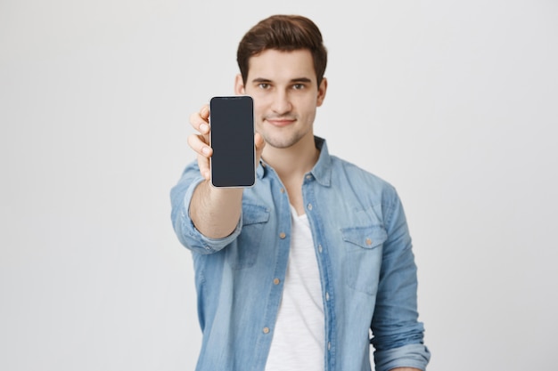 Beau jeune homme montrant smartphone