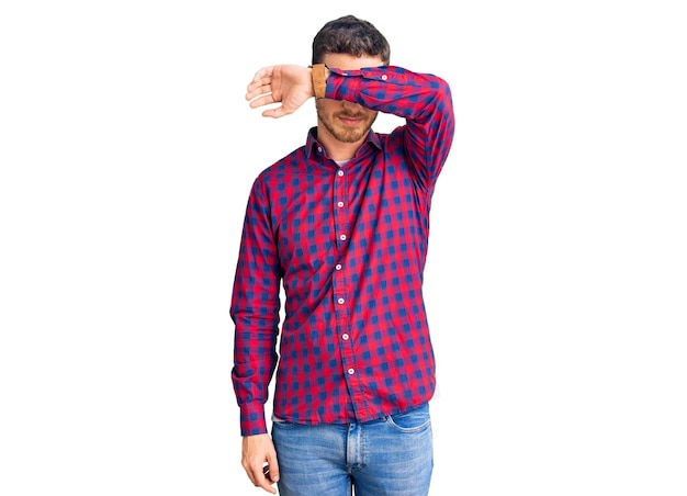 Photo gratuite beau jeune homme avec un ours portant une chemise décontractée couvrant les yeux avec le bras, l'air sérieux et triste. concept aveugle, de dissimulation et de rejet