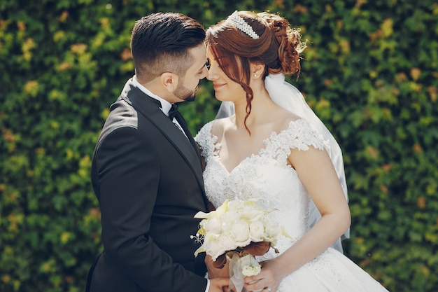 Un beau jeune homme portant un costume noir et une barbe dans le parc avec sa mariée