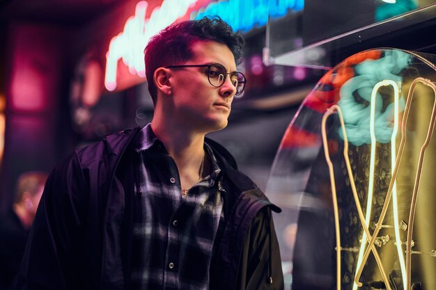 Un beau jeune homme portant un sweat à capuche de sport debout dans la rue la nuit. Enseignes lumineuses, néons, luminaires.