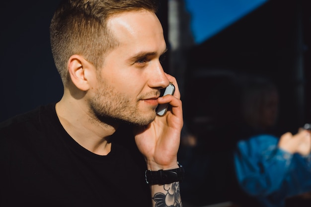 Beau jeune homme tatoué parlant au téléphone, portrait en gros plan, en plein air