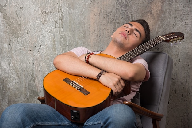 Beau jeune homme tenant la guitare et dormant sur la chaise.