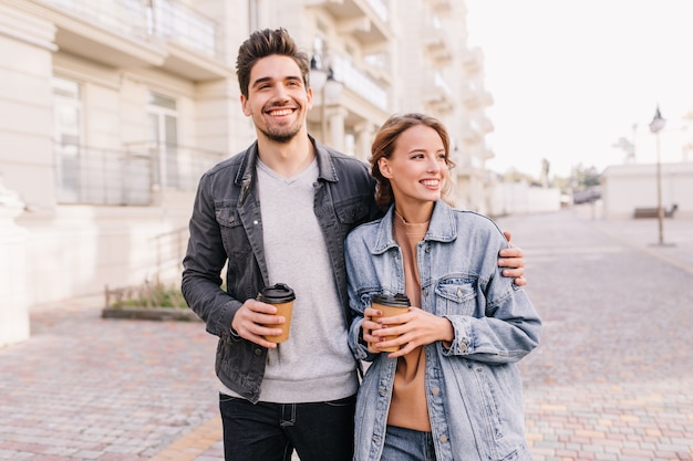 Beau jeune homme tenant une tasse de café et embrassant la petite amie. Couple souriant, appréciant la date en plein air.