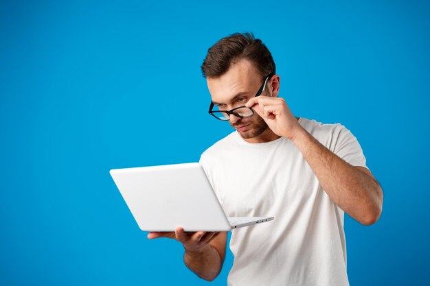 Beau jeune homme utilisant son ordinateur portable sur fond bleu