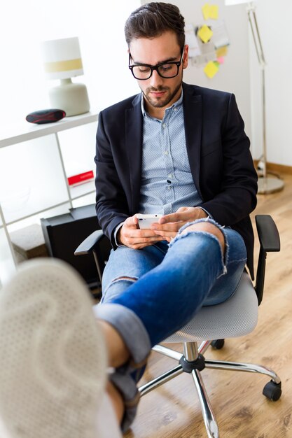 Beau jeune homme utilisant son téléphone portable au bureau.