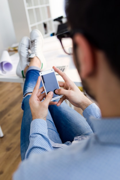 Beau jeune homme utilisant son téléphone portable au bureau.