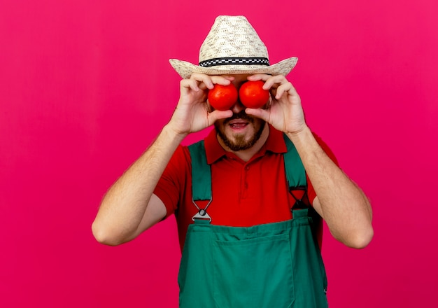 Photo gratuite beau jeune jardinier slave en uniforme et chapeau tenant des tomates devant les yeux