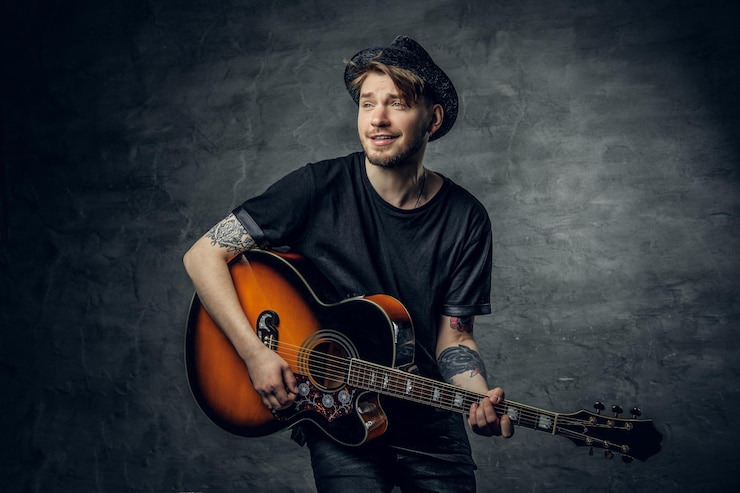Photo gratuit beau jeune joueur de blues de guitare acoustique avec des tatouages sur les bras exécutant ses compétences musicales.
