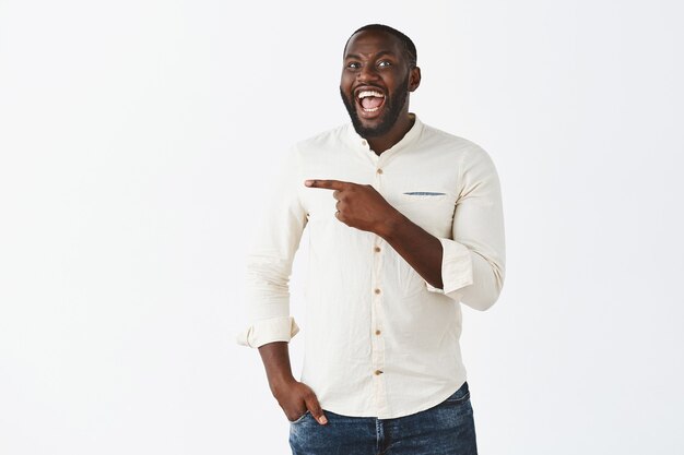 Beau jeune mec souriant posant contre le mur blanc