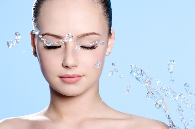 Beau jeune visage de femme propre avec des éclaboussures d'eau - fond bleu