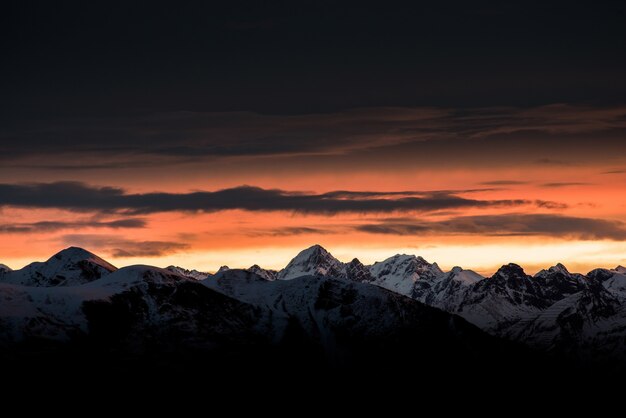 Beau lever de soleil à l'horizon avec de hautes montagnes et des collines enneigées et un ciel sombre incroyable