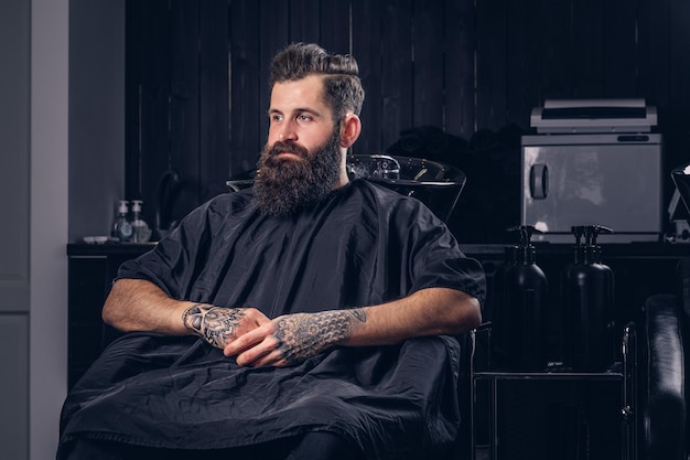 Photo gratuite beau mâle barbu avec un tatouage sur ses bras avant de se laver les cheveux dans un salon de coiffure.