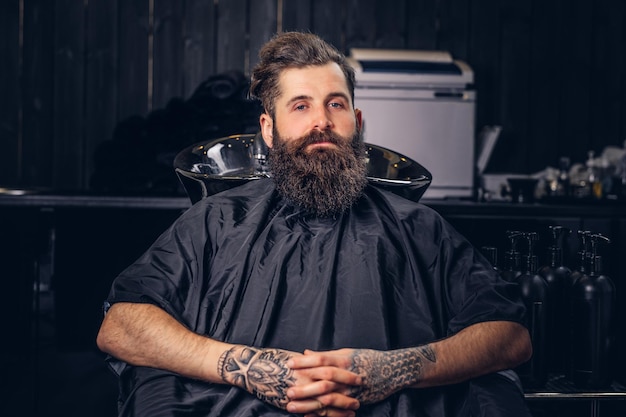 Beau mâle barbu avec un tatouage sur ses bras avant de se laver les cheveux dans un salon de coiffure.