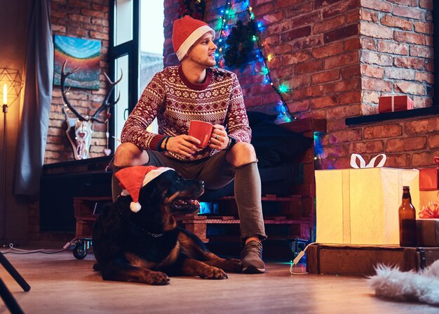 Beau mâle hipster barbu avec son chien Rottweiler dans une chambre avec décoration de Noël.