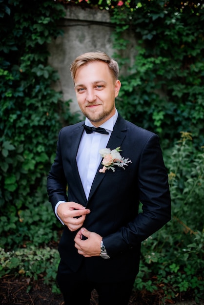 Photo gratuite beau marié en costume noir et fleur rose blanche à la boutonnière dans le jardin