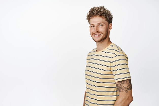 Beau mec blond souriant heureux à la caméra à la recherche de motivation et d'espoir debout dans une pose décontractée confiante sur fond blanc