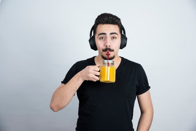 beau mec dans les écouteurs buvant dans une tasse en verre avec du jus d'orange.