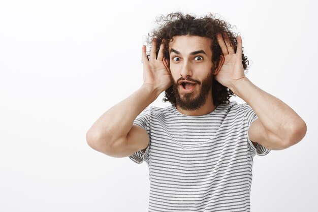 Beau mec excité intrigué qui aime les rumeurs intéressantes fraîches, tenant les paumes près des oreilles et laissant tomber la mâchoire par curiosité