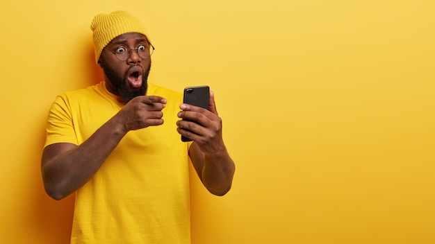 Beau mec nerveux avec des lunettes posant avec son téléphone