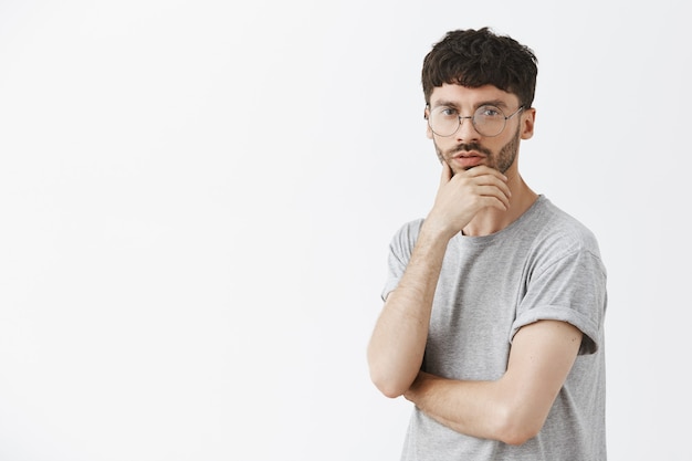 Beau mec réfléchi posant contre le mur blanc