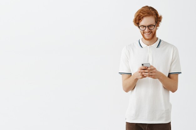 Beau mec rousse barbu posant contre le mur blanc avec des lunettes