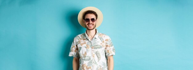 Beau mec souriant en lunettes de soleil et chemise d'été profitant de vacances en tournée debout sur le dos bleu