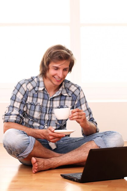 Beau mec avec une tasse de café et un ordinateur portable