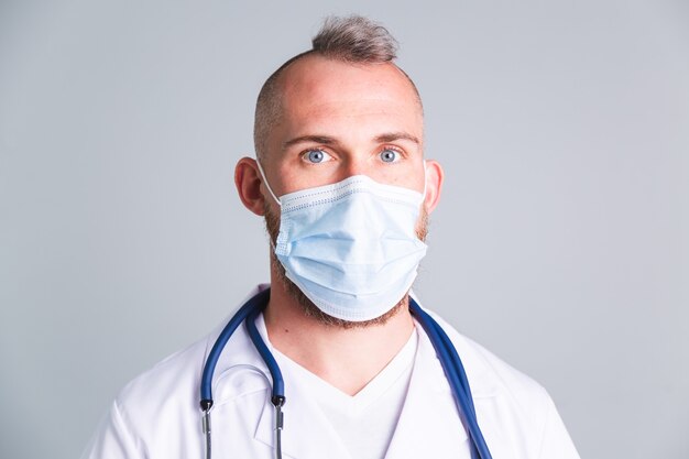 Beau médecin de sexe masculin sur mur gris avec masque médical protecteur sur le visage
