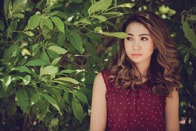 Un beau modèle asiatique qui pose au milieu des feuilles des arbres dans le parc