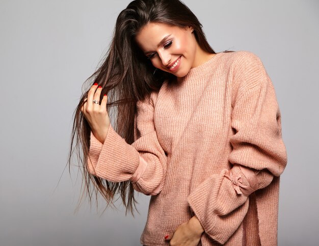 beau modèle brune en pull chaud beige décontracté jouant avec les cheveux